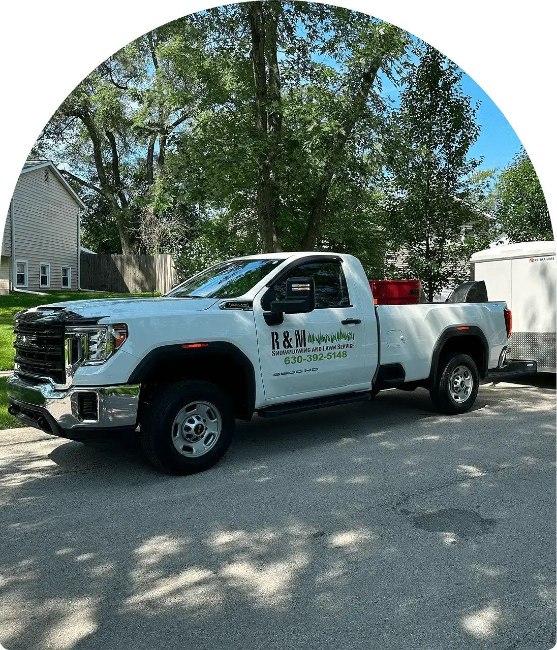 White truck with "R&M Handyman" logo, parked on a residential street, attached to a trailer. Trees and houses are in the background.